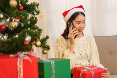 Noel konsepti, Asyalı bir kadının Noel 'de oturma odasında oturması ve akıllı telefondan konuşması..