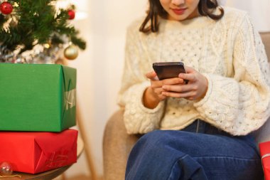Noel kutlaması konsepti. Genç Asyalı kadın oturma odasında oturmuş akıllı telefondan sohbet ediyor..