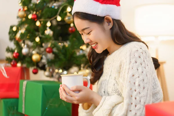 Christmas concept, Young asian woman holding coffee cup and sitting in christmas decorated room.
