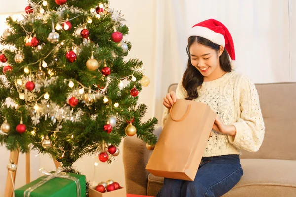 Noel kutlaması konsepti, Noel Baba şapkalı genç Asyalı kadın, gülümse ve yılbaşı hediyelerini aç..