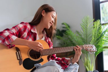 Hobby concept, Young asian woman learning and practice playing chords with acoustic guitar on couch.