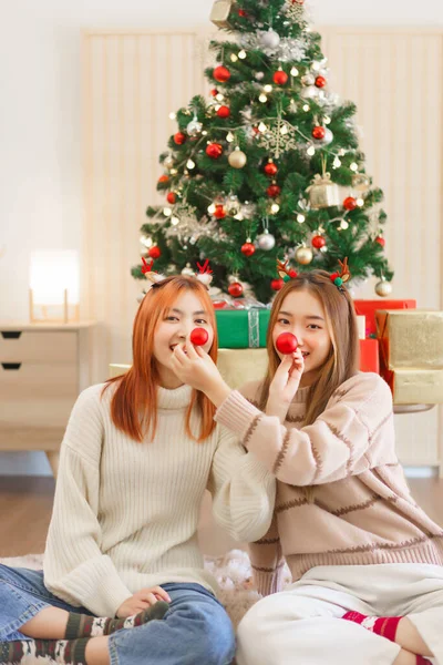 Christmas concept, Two women wears reindeer horns and cover nose with red christmas ball for friend.