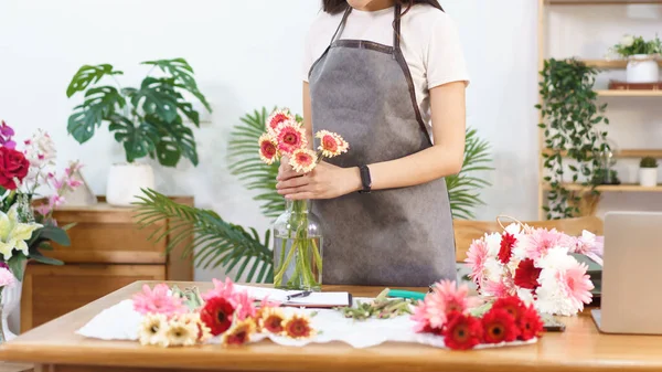 Flower shop concept, Female florist arranging colorful gerbera in vase on the table with happiness.