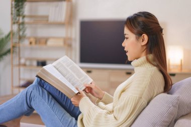 Rahatlatıcı zaman konsepti, kadın rahat koltukta uzanıp modern ev ofisinde kitap okuyor..