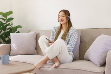 Rest time concept, Women sitting on comfortable the couch and wearing headphone to listening music.