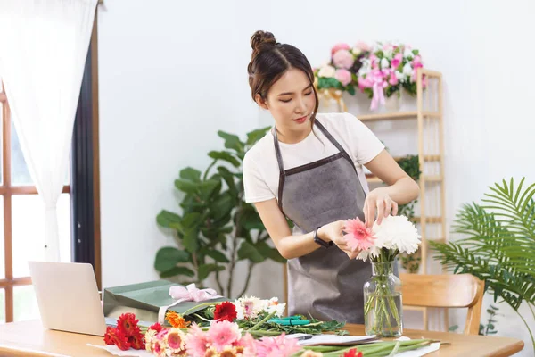 Florist concept, Female florist arranging pink gerbera and chrysanthemum in vase at flower shop.