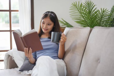 Work from home concept, Business women read a book and drink coffee while lying on couch to relax.