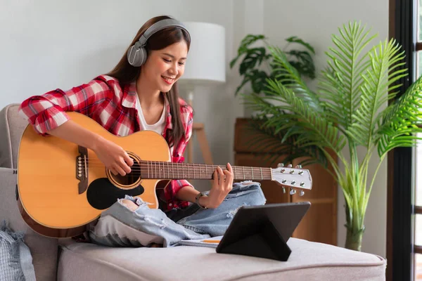 Concept of relaxation with music, Young woman plays acoustic guitar while learning music on tablet.
