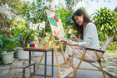 Artist concept, Female artist use brush to mix color on palette for painting on canvas in garden. clipart