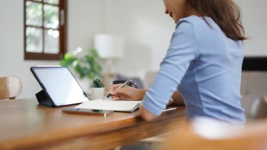 Work from home concept, Business women reads financial data on tablet and taking notes in notebook.