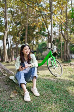 Ağaçların altında oturan kadınlar parkta bisiklet sürdükten sonra internetten izleyip akıllı telefonlarda sörf yapıyorlar..
