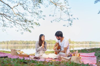 Akustik gitar çalan genç bir adam ve kız arkadaşı şarkı söylerken mikrofon olarak tahta kaşık kullanıyor..
