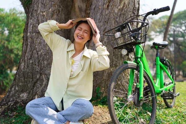 공원에서 자전거를 휴식을 취하는 아래앉아 책으로 머리를 가리는 여성들 — 스톡 사진