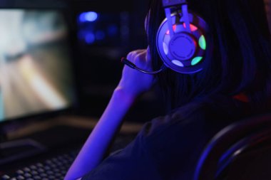 Kadın bilgisayar korsanı kulaklıkla oyun oynamaya ya da programlama sistemini hacklemeye ciddi bir yüz ifadesi.