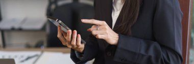 Sekreter konsepti, kadın sekreter akıllı telefon üzerinde çalışıyor ve ofisin penceresinin yanında duruyor..