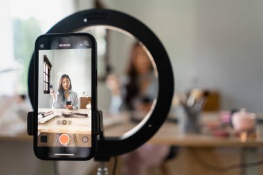 Güzellik blogcusu makyaj vlog kaydedicisi için akıllı telefondan video kaydederken toz ürününü gözden geçiriyor.