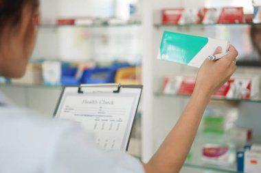 Medicine and health concept, Female pharmacist hold medicine box to checklist in paper at drugstore.