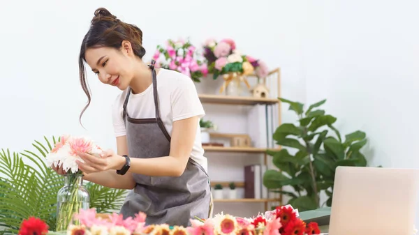 Florist concept, Female florist arranging colorful flowers in vase with happiness in flower shop.