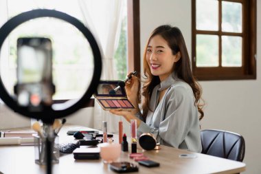 Güzellik blogcusu makyaj vlog kaydedicisinde kozmetik incelemesi için ürünleri gösterme fırçasını kızartarak tut.