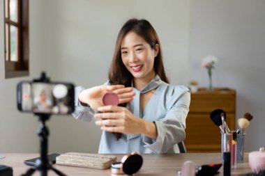 Güzellik blogcusu allık tutuyor ve makyaj vlogger kozmetik gözden geçirmek için ürün gösteriyor.