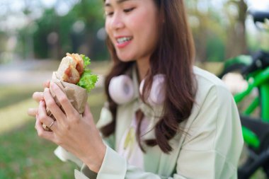 Parkta bisiklet sürdükten sonra çimenlerin üzerinde dinlenirken kadınlar mutlulukla sandviç yiyorlar..