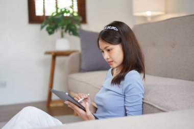 Work from home concept, Business women sit on the floor in living room and writing data on tablet.