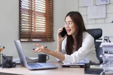 İş konsepti, İş kadını bilgisayardaki verileri okurken akıllı telefondan partneriyle konuşuyor.