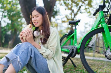 Parkta bisiklet sürdükten sonra çimenlerin üzerinde dinlenirken kadınlar mutlulukla sandviç yiyorlar..