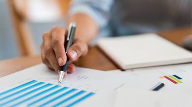Not defterine notlar yazmak için çalışan ve finansal belgeleri okuyan iş kadınlarının ellerini kapat.