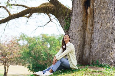 Kadınlar ağaçların altında huzur içinde otururken parkta doğa manzarası ve rahatlığı izliyorlar..