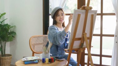 Genç kadın ressam, ev stüdyosunda keyif alarak tuval üzerine resim çizer ve resim yapar..