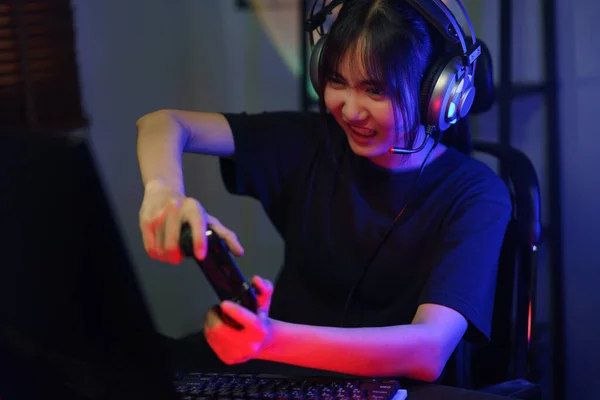 女黑客在耳机里用霓虹灯下的操纵杆在计算机上玩电子游戏 — 图库照片