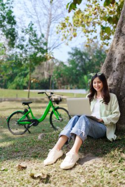 Ağaçların altında oturan kadınlar parkta bisiklet sürdükten sonra dizüstü bilgisayarlarıyla sosyal medyada geziniyorlar..