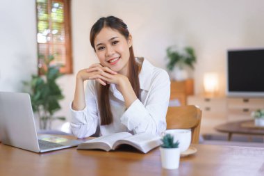 Rahatlatıcı zaman kavramı, modern ev ofisinde çalıştıktan sonra gülümseyerek kitap okuyan kadın..