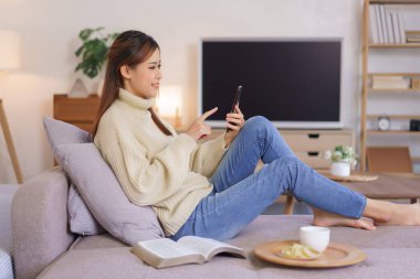 Rahatlatıcı zaman konsepti, kadınlar modern ev ofisteki akıllı telefondan online alışverişe kanepede oturur..