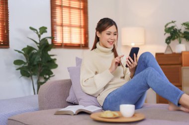 Rahatlatıcı zaman konsepti, kadınlar modern ev ofisteki akıllı telefondan online alışverişe kanepede oturur..