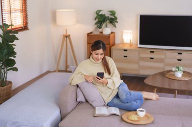 Relaxing time concept, Women sit on couch to surfing social media on phone in modern home office.