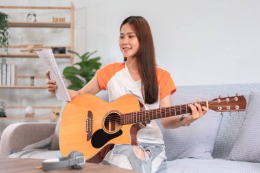 Hobi konsepti, genç kadın kanepede oturup şarkı sözleri okuyup akustik gitarla müzik çalıyor..