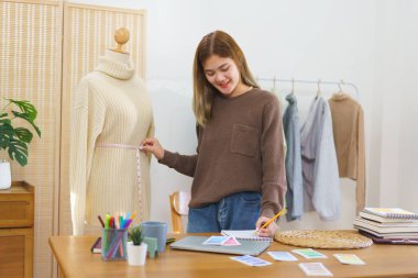 Fashion design concept, Fashion designer measuring sweater in mannequin and taking notes to checkup.