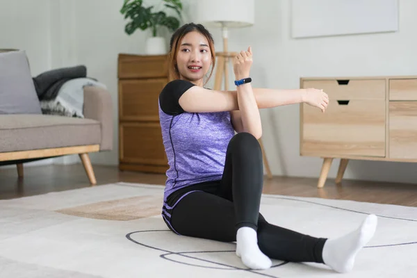 若いアジアの女性は自宅で健康的なライフスタイルをトレーニングするために床に腕を伸ばすために運動をする — ストック写真
