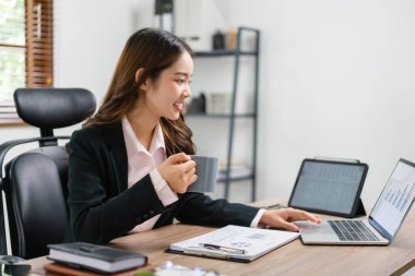İş kadını kahve içerken dizüstü bilgisayardan pazarlama planını okuyor..