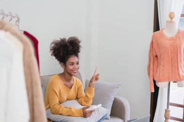 Afrikalı Amerikalı moda tüccarı kadın canlı yayında online kıyafet satmak için akıllı telefon kullanıyor..