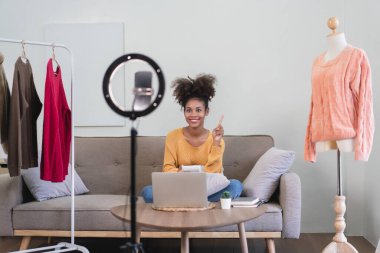 Afrikalı Amerikalı moda tüccarı kadın canlı yayında online kıyafet satmak için akıllı telefon kullanıyor..