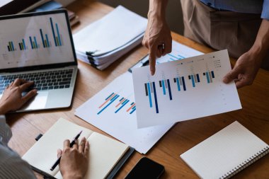 Finansal döküman grafiğine işaret eden işadamlarına ve dizüstü bilgisayarda yazan iş kadınlarına yakın dur..