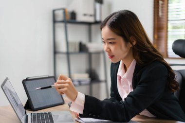 İş kadını finans belgesini okuyor ve dizüstü bilgisayarda yeni başlatılan projenin pazarlama planını kontrol ediyor.