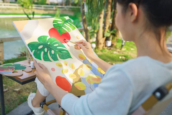 Creative art concept, Female artist sitting in park and painting picture on canvas with happiness.