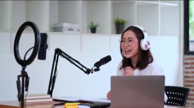 Genç Asyalı kadın sunucu ya da DJ abonelerle konuşuyor ses yayını yapıyor ya da konuşuyor ses yapıyor, mikrofon kullanıyor ve kulaklık takıyor, yayın yapıyor 