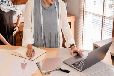 Asyalı terzi kadınlar dizüstü bilgisayarda moda koleksiyonu ve çizim için verileri kontrol ediyorlar..