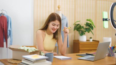 Online merchant concept, Fashion designer holds pencil to checklist online cloth order in notebook.