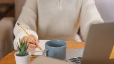 Home lifestyle concept, Young woman working on laptop and writing data in notebook at late night.